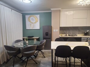A modern kitchen with a refrigerator, sink, and dining area with chairs and a table. - Sandton Westpoint Luxury Apartments 172 (Sandton)