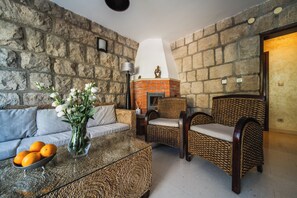 Una sala de estar con pared de piedra, chimenea, sofá, mesa de centro con naranjas y sillas de mimbre.