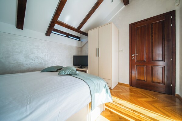 A bedroom with a bed, a television on a stand, a wardrobe, and a wooden door.