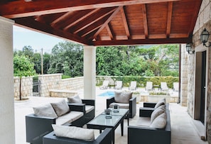 An outdoor patio with wicker furniture, a glass table, and a stone wall.