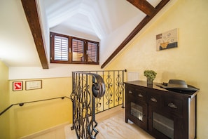 Un escalier orné de rampes en métal ouvragé, un plafond en bois et une fenêtre à volets.