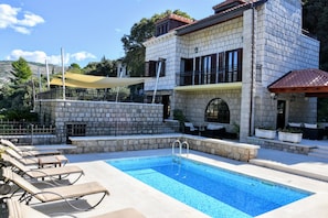 A pool area with lounge chairs, a stone building with balconies, and a clear blue sky. - Villa Franica (Dubrovnik)