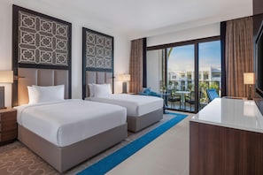 Une chambre d’hôtel avec deux lits, un bureau et un balcon donnant sur des immeubles.