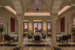 Un comedor amplio con techos altos, ventanas grandes y vista a la playa al atardecer.