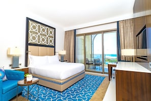 Habitación de hotel con una cama grande, un escritorio, un sofá y un balcón con vistas al océano.