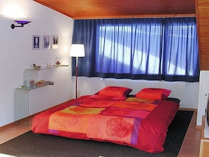 A bedroom with a bed, a nightstand, a lamp, a window with curtains, and a radiator. - Pierenhus Appartement/Fewo, Dusche, WC, Balkon 2-Zimmerwohnung by Interhome (Adelboden)