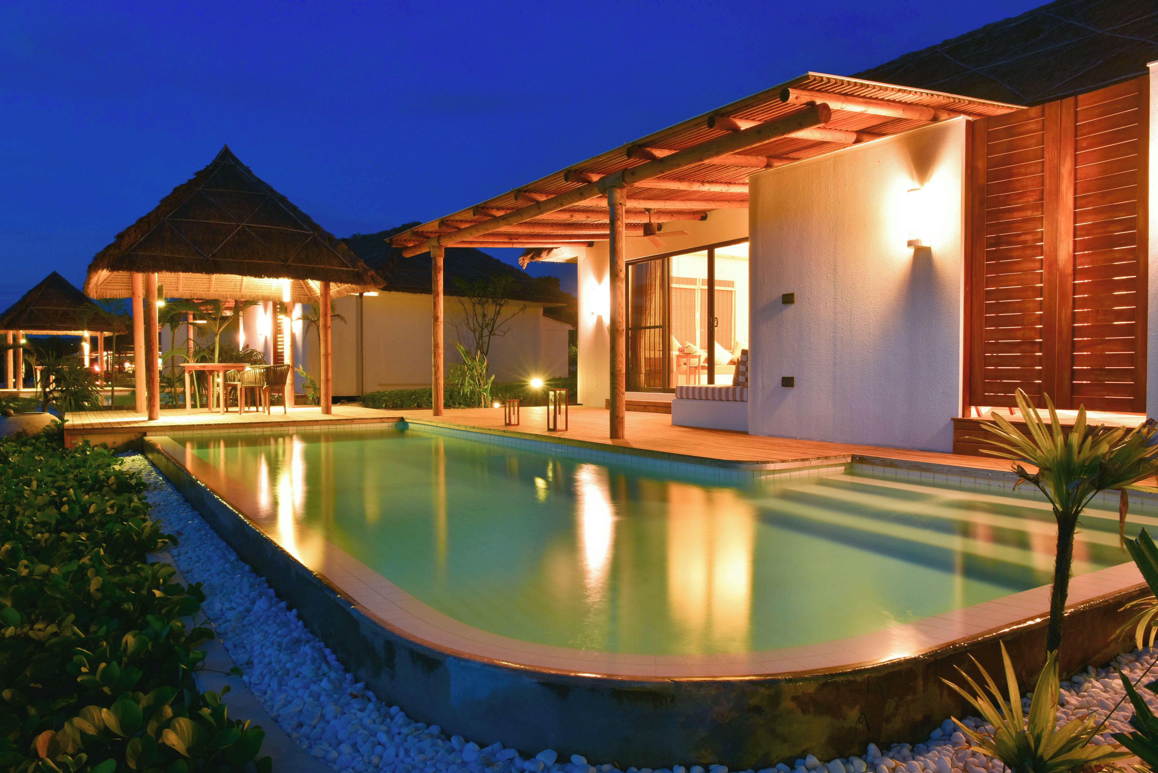 A resort with a swimming pool, covered outdoor seating, and a thatched-roof structure.