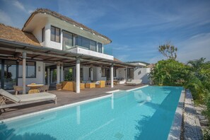 Een modern huis met een zwembad, terras en rieten dak.