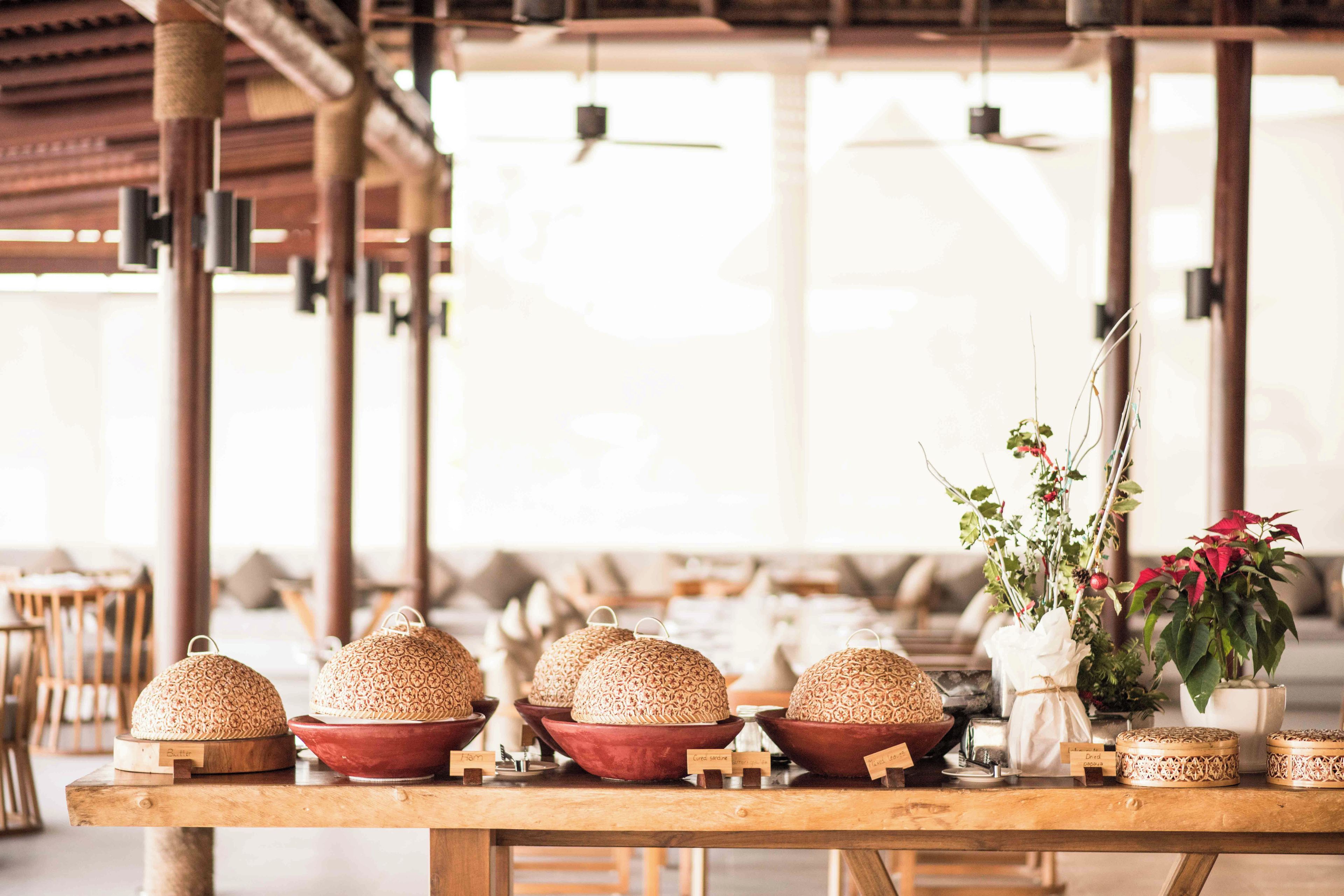 A wooden table with woven baskets and a potted plant with red flowers.
