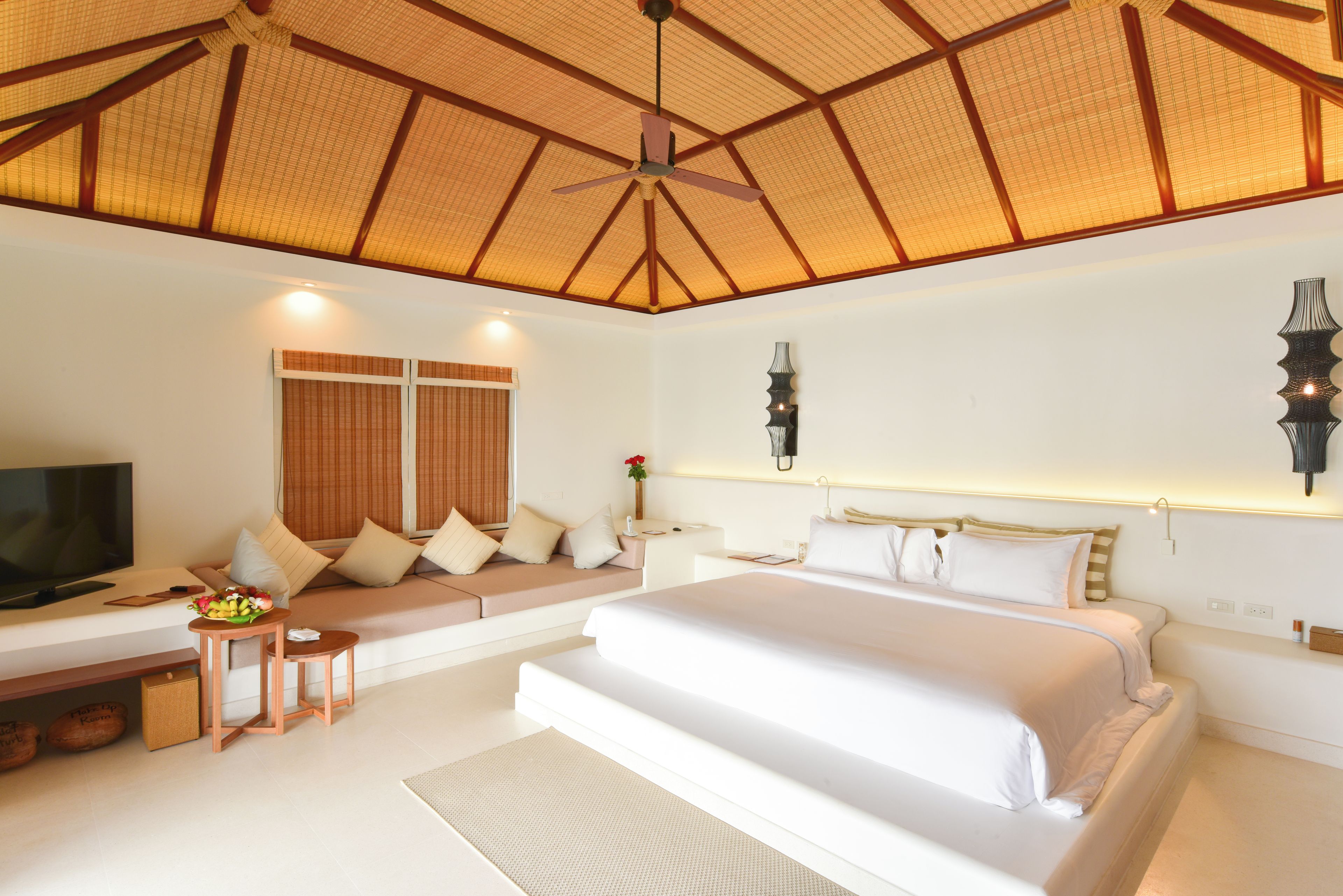 A bedroom with a large bed, a TV, a seating area, and a ceiling fan.