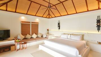 A bedroom with a large bed, a TV, a seating area, and a ceiling fan.