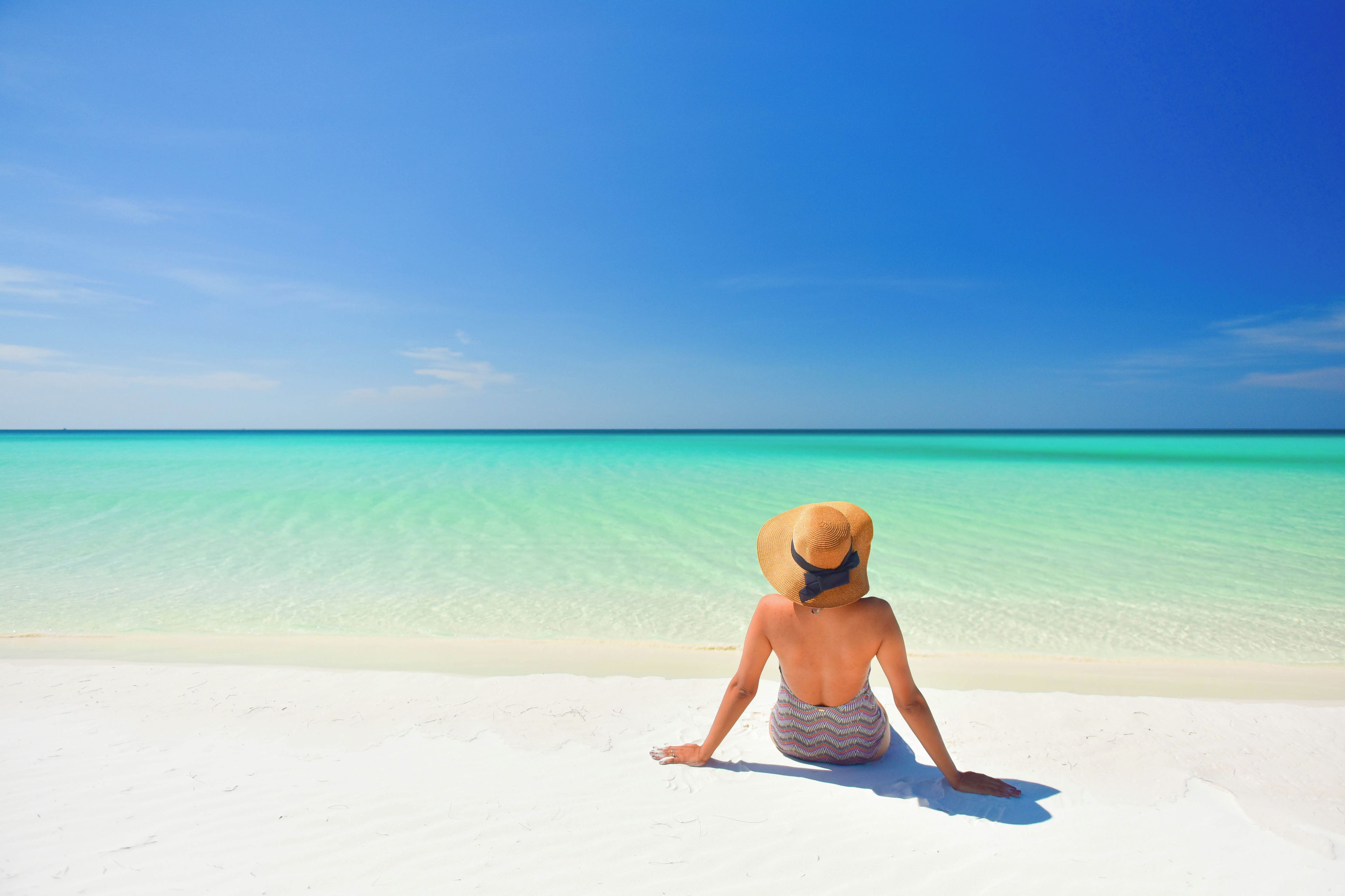 A person sitting on a sandy beach facing a clear blue sea.