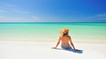 A person sitting on a sandy beach facing a clear blue sea.
