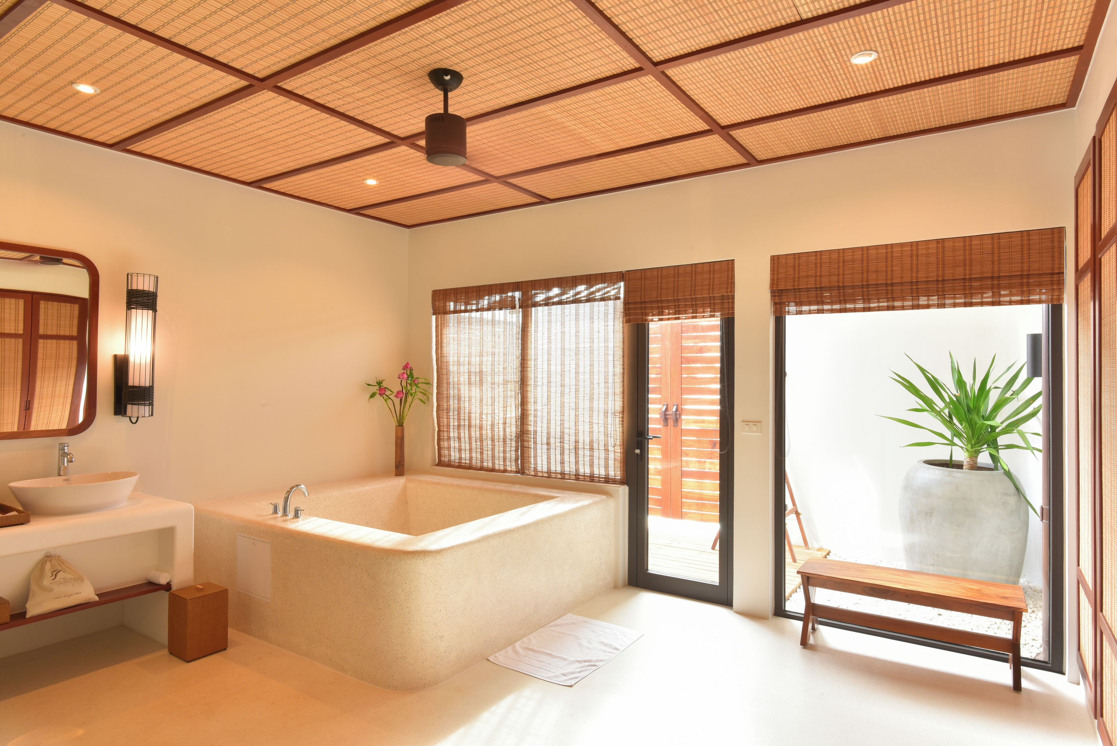 A modern bathroom with a large bathtub, a sink, a bench, and a potted plant.