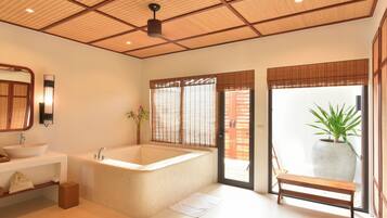 A modern bathroom with a large bathtub, a sink, a bench, and a potted plant.