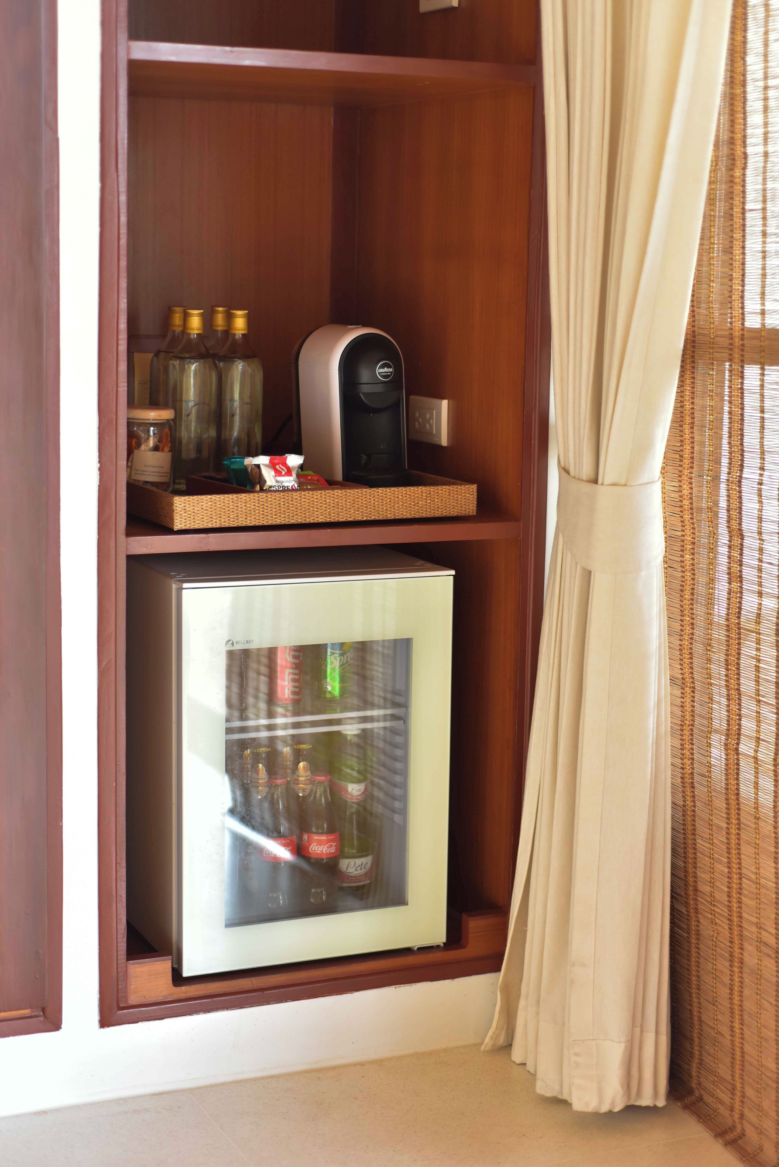 A minibar with a coffee maker, bottles, and a refrigerator containing beverages.
