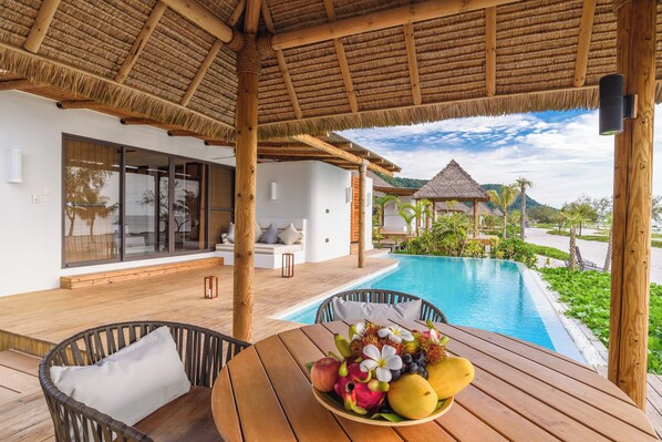 A wooden deck with a thatched roof, a pool, and a table with fruit. - The Royal Sands Koh Rong (Sihanoukville)