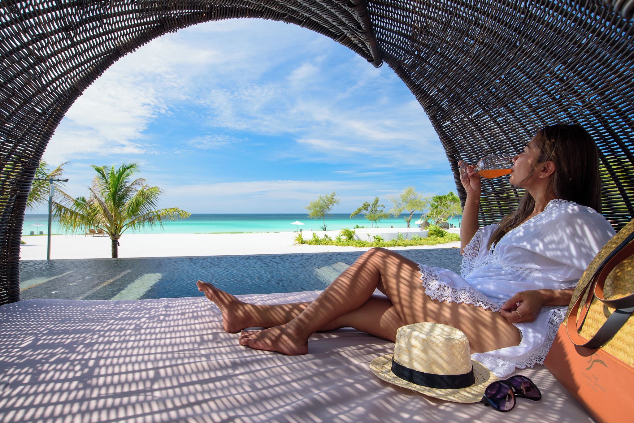A person relaxing on a wicker lounge chair with a view of a beach and ocean.