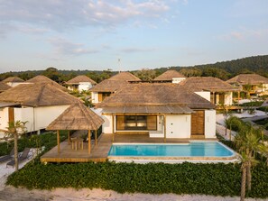 Un resort con cabañas de techo de paja, piscina y vista al mar.