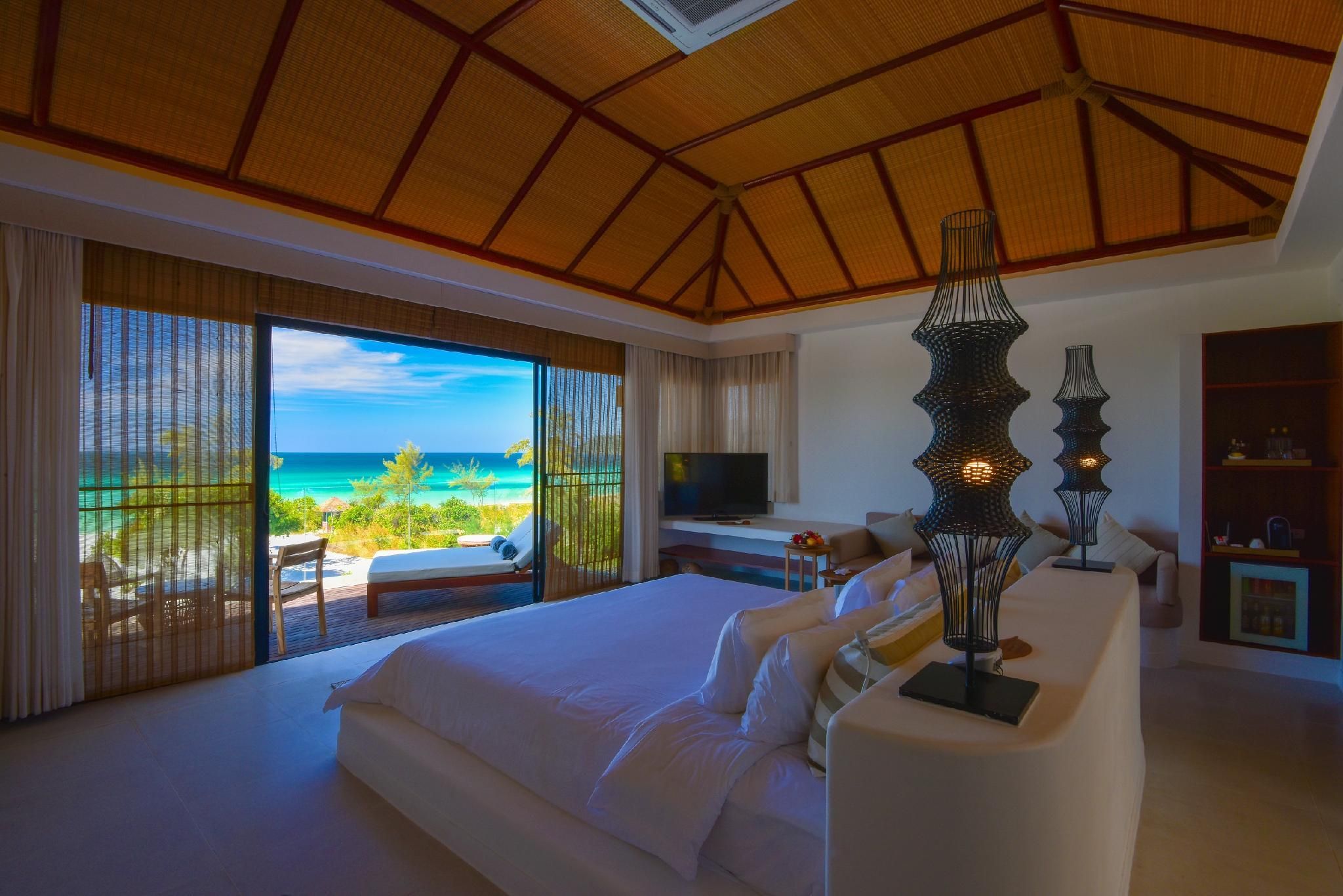 A bedroom with a large bed, a TV, and a view of the ocean.
