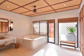 Een moderne badkamer met een vrijstaand bad, een grote spiegel en een bankje bij de ingang.