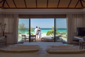 Habitación de hotel con una ventana grande, una cama, un televisor y un área de comedor con vista al océano.