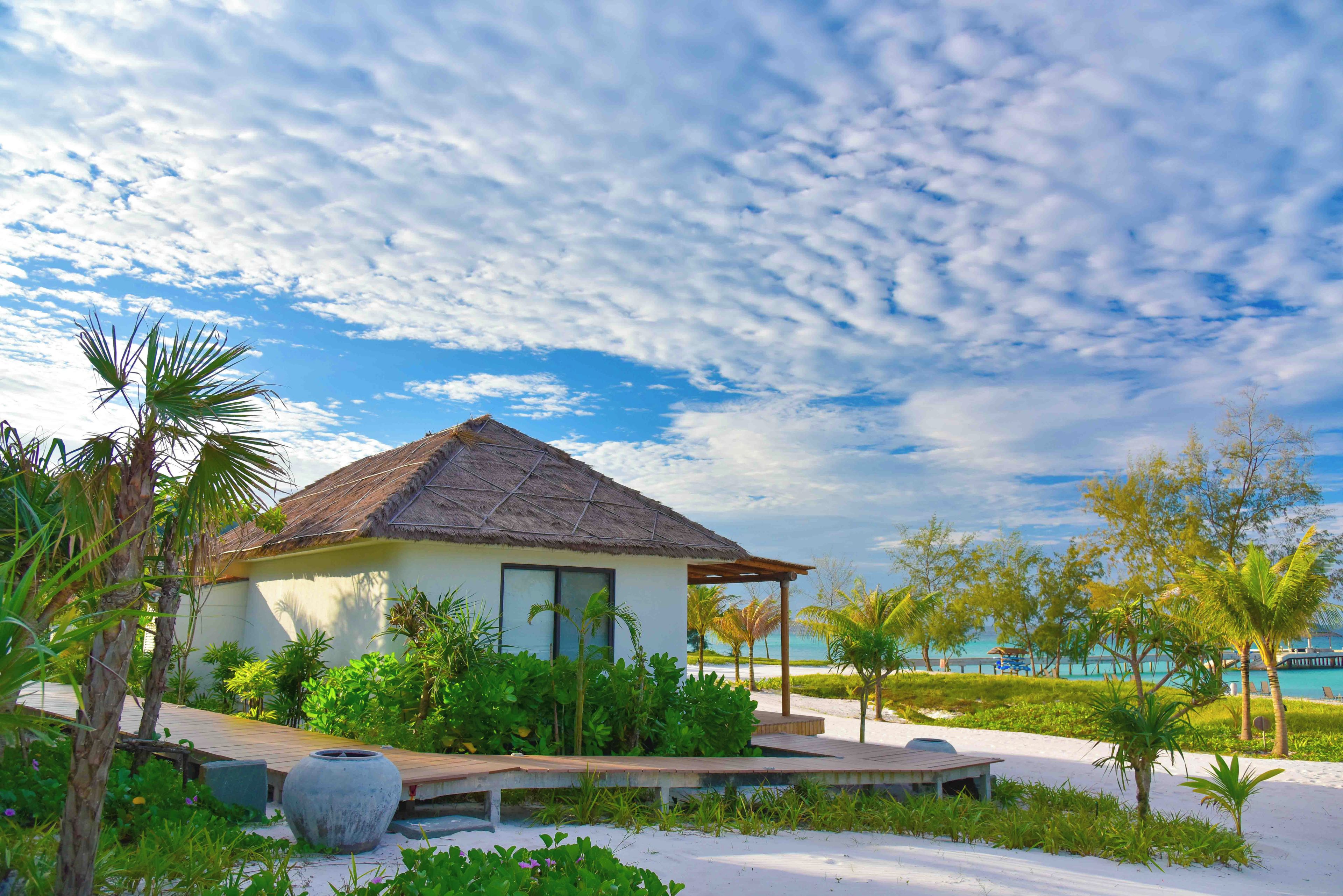 A beachfront property with a thatched-roof building, a wooden deck, and a sandy beach.