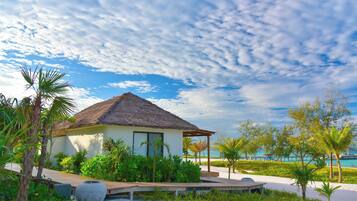 A beachfront property with a thatched-roof building, a wooden deck, and a sandy beach.