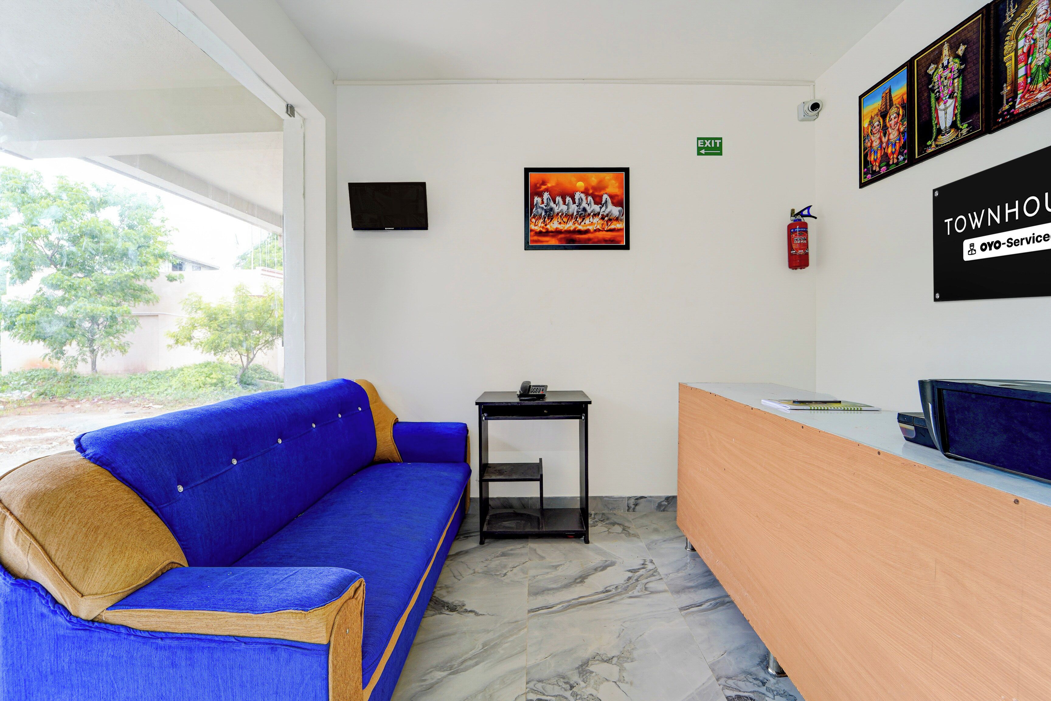 A reception area with a blue sofa, a small table, a flat-screen TV, and a fire extinguisher.