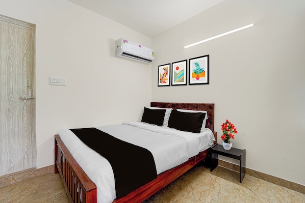 A neatly made bed with a black and white bedspread, a wooden headboard, and a nightstand with a vase of flowers.