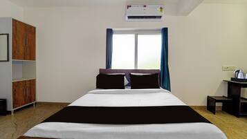 A hotel room with a bed, a wardrobe, a desk with a kettle, and an air conditioning unit.