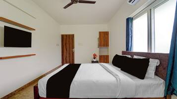 A bedroom with a bed, a ceiling fan, a TV mounted on the wall, a window with curtains, and a wooden door.