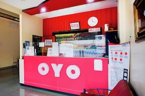 A reception desk with a clock, signs indicating COVID-19 safety measures, and a menu board. - Collection O Banda Aceh Near Masjid R Baiturrahman (Banda Aceh)