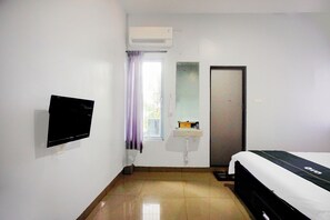 Una habitación con cama, televisión montada en la pared, ventana con cortinas, lavamanos y aire acondicionado.