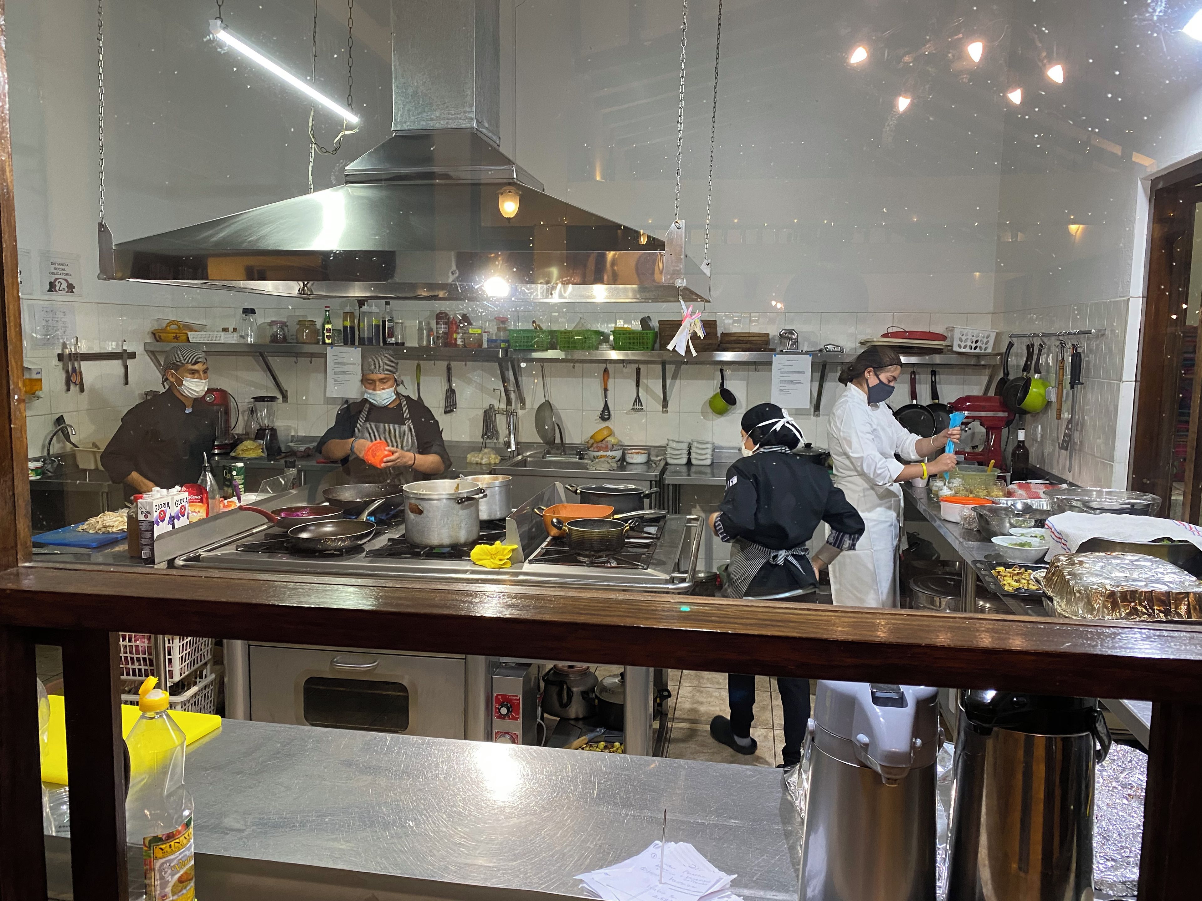 A commercial kitchen with stainless steel appliances, hanging utensils, and chefs at work.