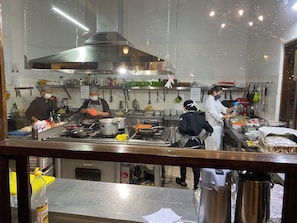 Una cocina comercial con electrodomésticos de acero inoxidable, utensilios colgando y cocineros trabajando.