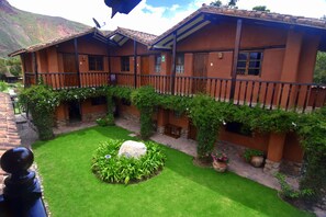 A traditional wooden house with a balcony, a stone wall, and a well-maintained garden with a large rock centerpiece.