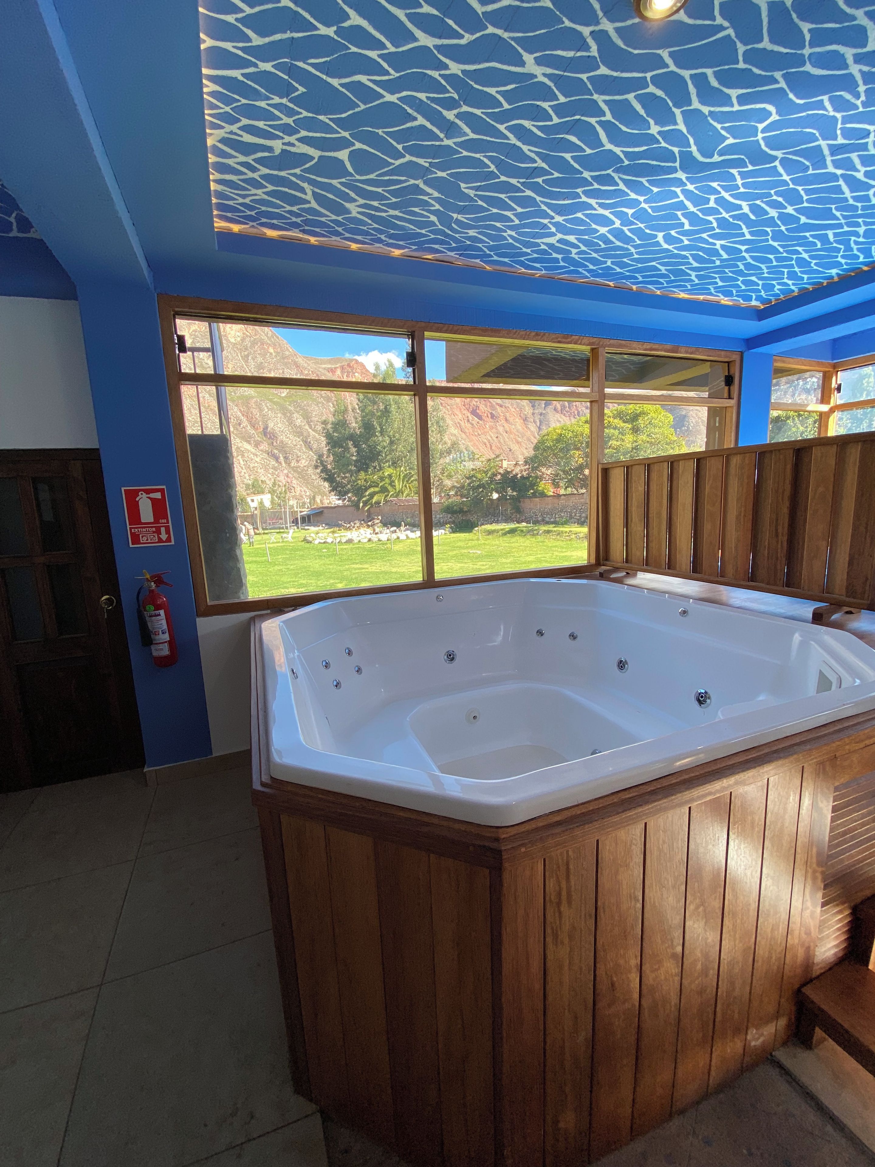 A room with a wooden bathtub, a fire extinguisher, and a window with a view of a mountainous landscape.