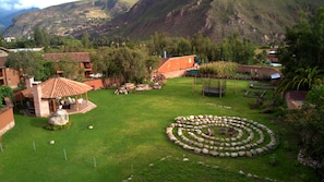 Un jardín exuberante con un conjunto circular de piedras, un pabellón y vistas a un paisaje montañoso.