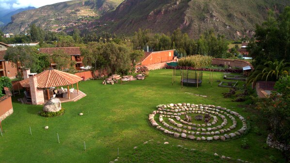 A lush garden with a circular stone arrangement, a gazebo, and a view of a mountainous landscape.