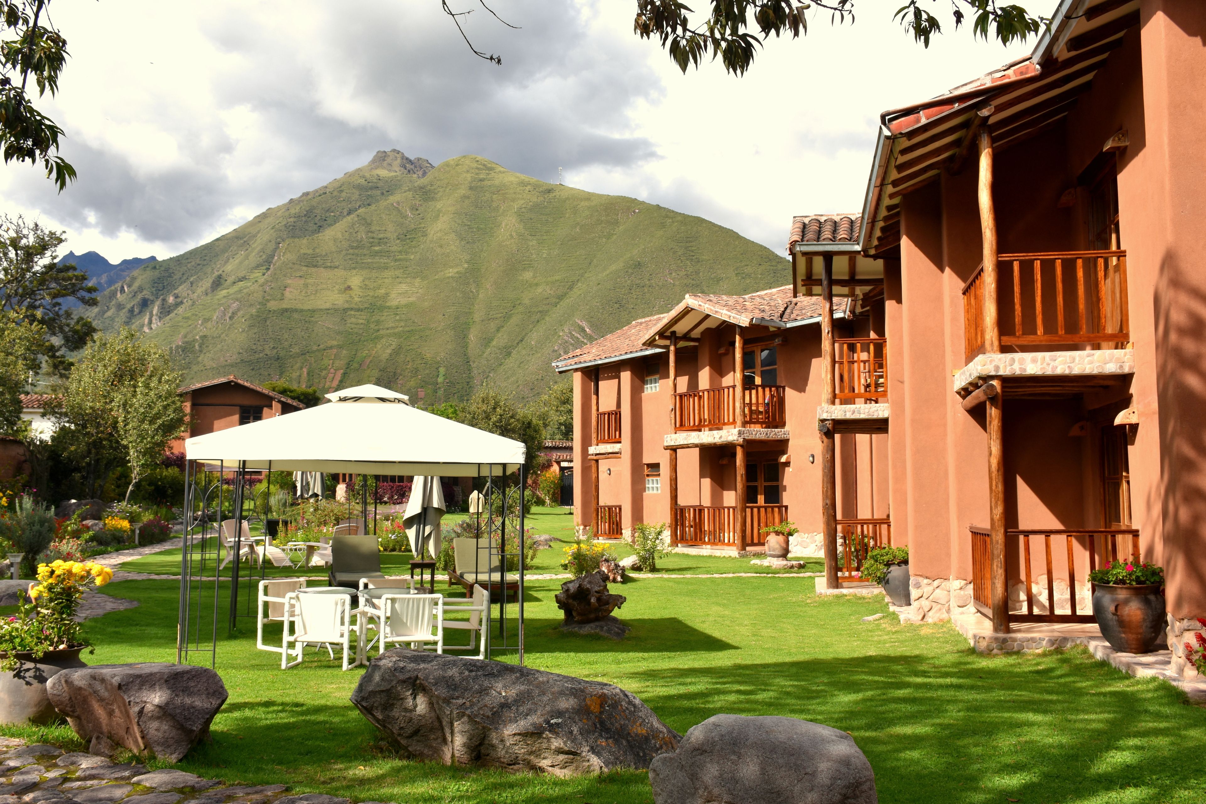 Un patio de hotel con mobiliario exterior, montañas al fondo y arquitectura tradicional.