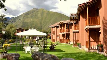 Un patio de hotel con mobiliario exterior, montañas al fondo y arquitectura tradicional.