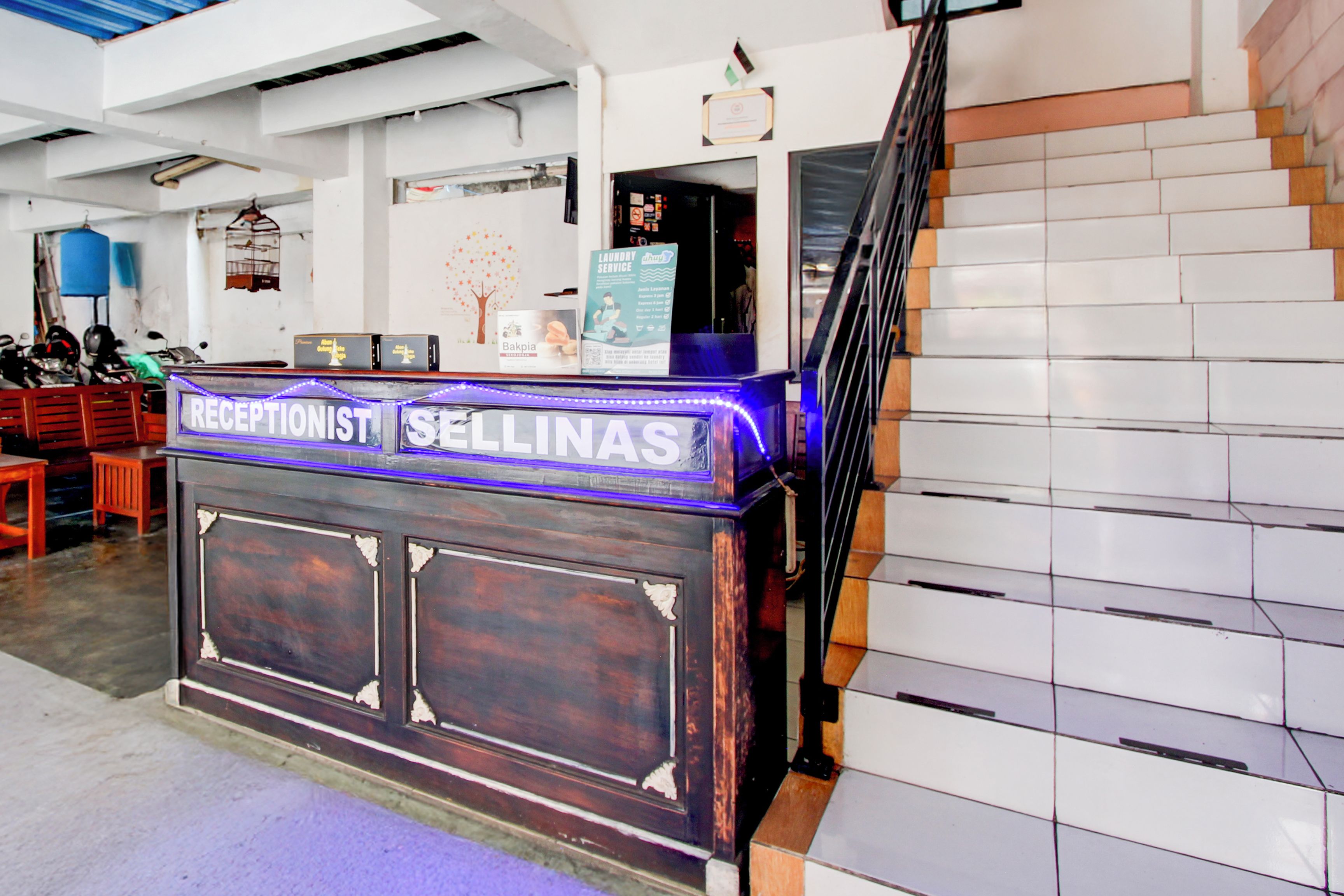 Ein Empfangsschalter mit einem Schild, auf dem 'RECEPTIONIST SELINAS' steht, und ein Treppenhaus zur Rechten.