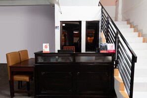 Ein Empfangsschalter mit einem Holztisch und Stühlen, eine Treppe mit schwarzem Gel änder und eine weiße Wand mit einer Tür zu einem anderen Raum.