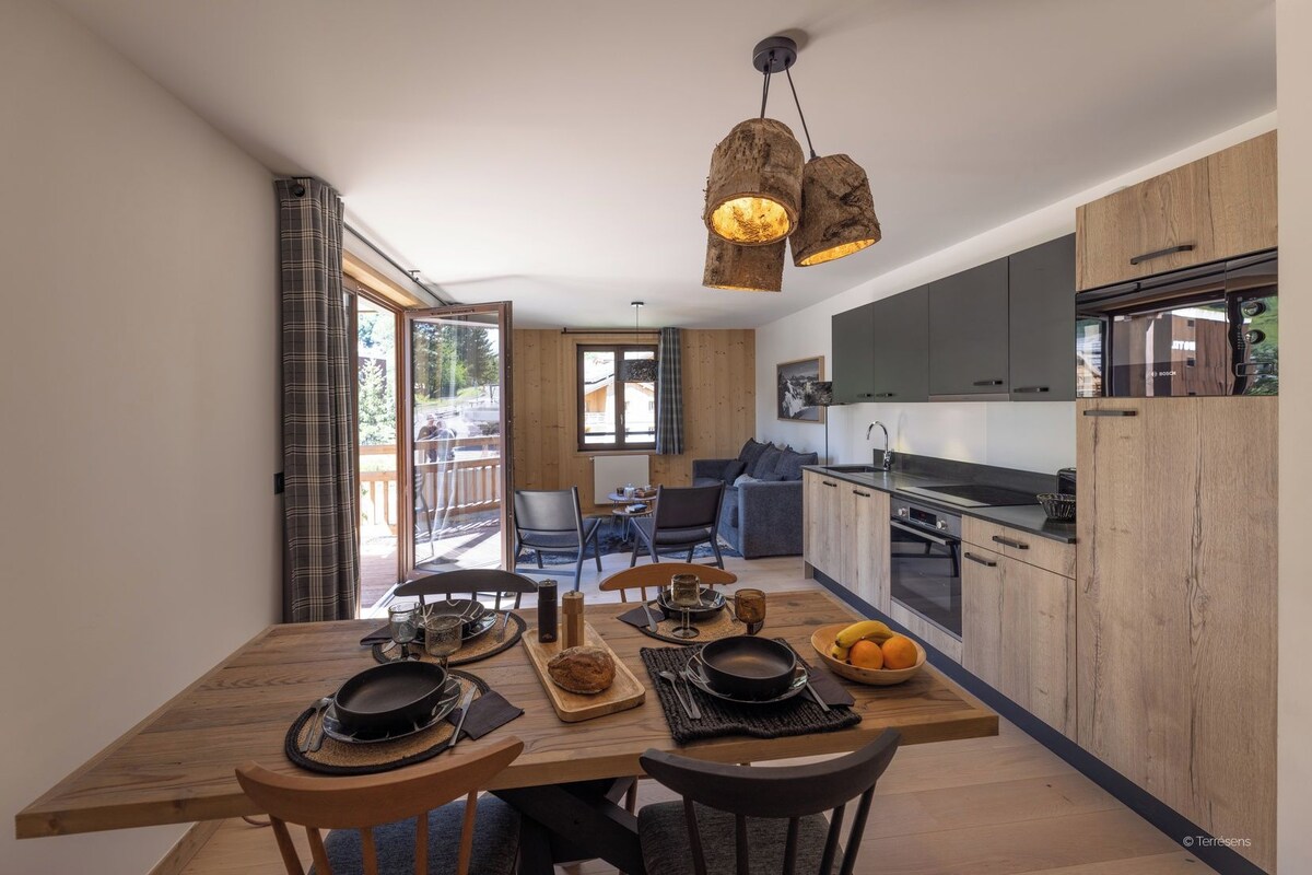A modern kitchen with wooden cabinets, a dining area with a wooden table, and a view of the outdoors.