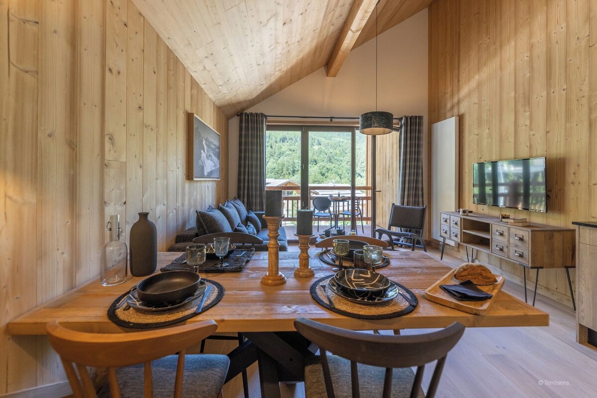 A wooden interior with a dining table set for four, a sofa, and a TV mounted on the wall.