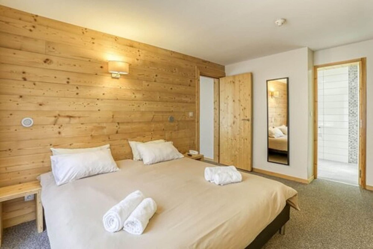 A hotel room with a wooden headboard, a bed with white linens, a bedside table, and a mirror.