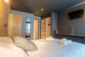 A hotel room with a bed, a wardrobe, a mirror, and a shelf with items.