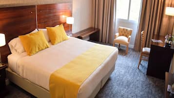 Habitación de hotel con una cama grande, dos mesitas de noche, una silla, un escritorio y un ventanal con cortinas.