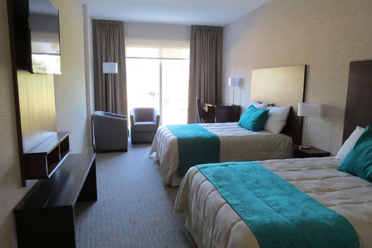 Habitación de hotel con dos camas, un escritorio, una silla y un televisor.